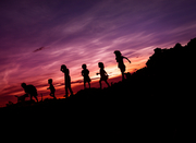 Umrisse von einer Gruppe von Kindern, die vor einem lila-roten Himmel laufen oder spielen und von denen nur die Umrisse zu sehen sind. 