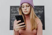 Jugendliches Mädchen steht vor Tafel und schaut auf ihr Handy