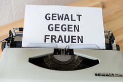 Schreibmaschine mit weißem Papier, auf dem in Großbuchstaben "GEWALT GEGEN FRAUEN" geschrieben steht